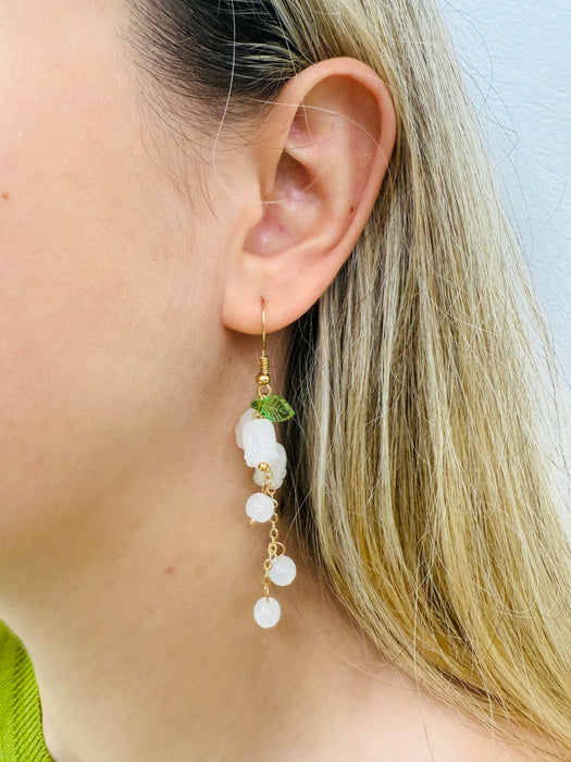 A pair of elegant drop earrings with frosted white floral beads, translucent accents, and green leaf details, on a gold-colored chain.