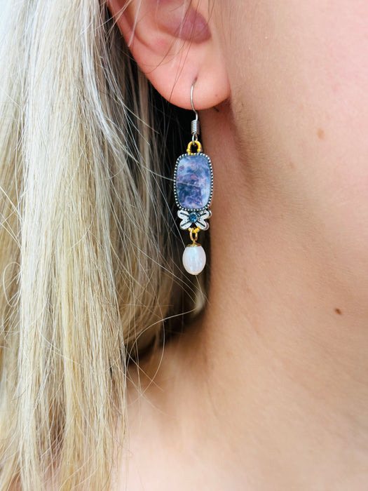 A delicate pair of dangle earrings with purple teardrop-shaped stones and pearl drops.