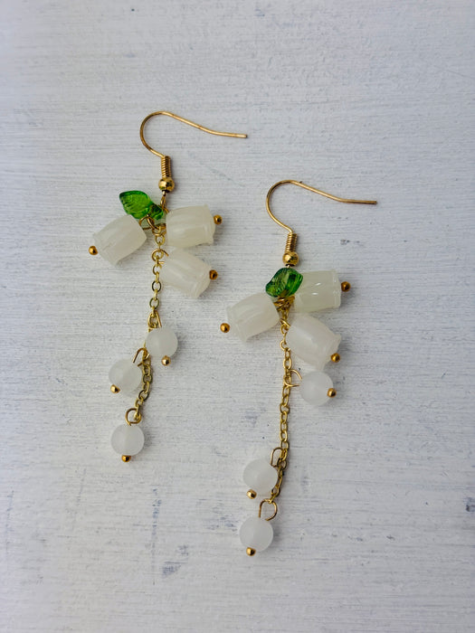 A pair of elegant drop earrings with frosted white floral beads, translucent accents, and green leaf details, on a gold-colored chain.
