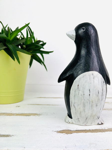 front view of wood penguin on wooden surface next to a plant pot