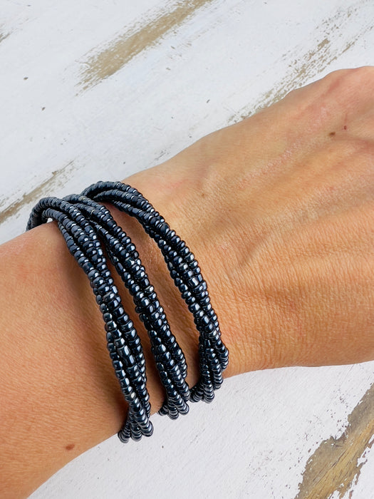 A gunmetal-coloured seed bead bracelet with a plaited effect and shell detail at each end, displayed on a model.