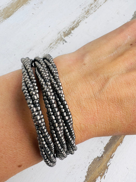 A silver metallic seed bead bracelet with a plaited effect and shell detail at each end, displayed on a model.