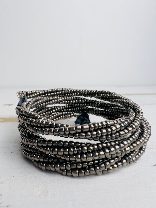A silver metallic seed bead bracelet with a plaited effect and shell detail at each end, displayed on a light background.