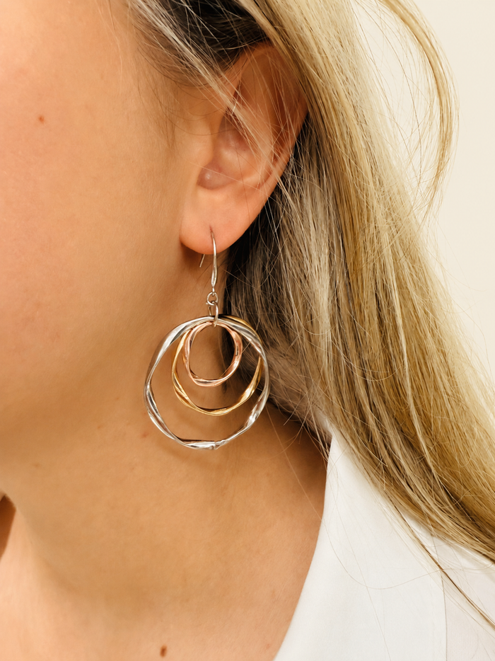 A close-up image of a woman's ear wearing a silver and gold tone interlocking rings dangle earring.