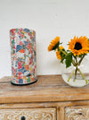 display view of glass mosaic cylinder next to vase of sunflowers