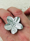 Adjustable silver-tone statement ring featuring a five-petal flower with textured detail, displayed on a model.