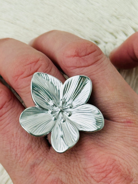 Adjustable silver-tone statement ring featuring a five-petal flower with textured detail, displayed on a model.