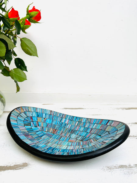 front view of mosaic oval bowl next to a vase of flowers on white background