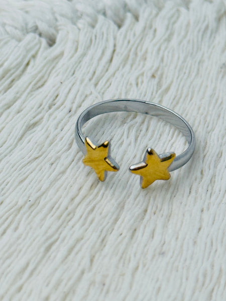 Twin star adjustable ring with two gold-tone stars on a silver-tone open band, displayed on a white fabric background.