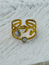 Gold celestial harmony ring with crescent moon, star, sun and moonstone-effect cabochons on an open band, displayed on a white fabric background.