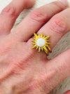 Gold sunburst ring with moonstone-effect acrylic cabochon on open band, displayed on a model.