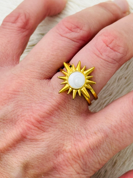 Gold sunburst ring with moonstone-effect acrylic cabochon on open band, displayed on a model.