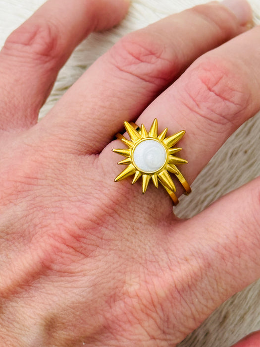 Gold sunburst ring with moonstone-effect acrylic cabochon on open band, displayed on a model.