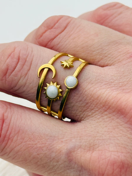 Gold celestial harmony ring with crescent moon, star, sun and moonstone-effect cabochons on an open band, displayed on a model.