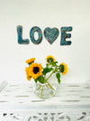 display view of love mosaic wall art on the wall with vase of flowers on table below