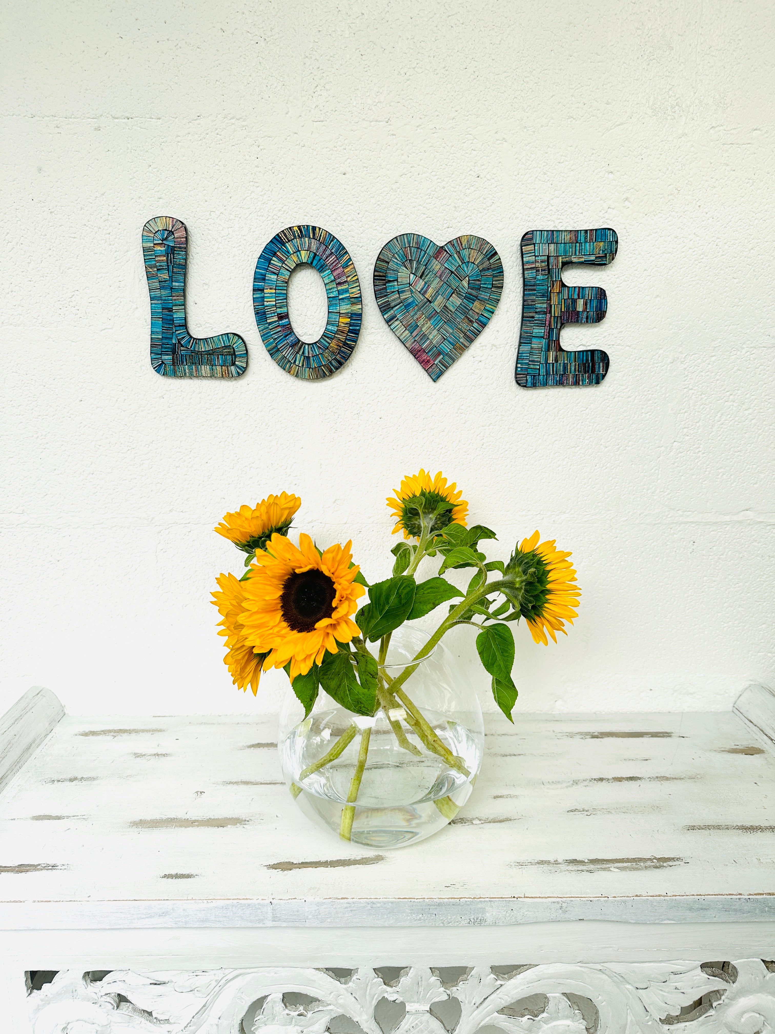 display view of love mosaic wall art on the wall with vase of flowers on table below