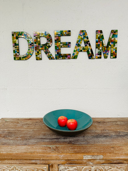 display view of mosaic 'DREAM' on a white background with a bowl of apples on a wooden surface below
