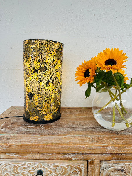 display view of mosaic cylinder lamp next to a vase of sunflowers on wooden surface