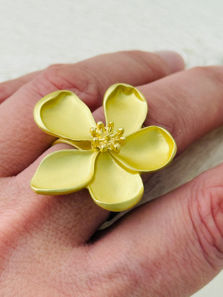 Adjustable statement ring with matte gold-tone five-petal flower and textured centre, displayed on a model.