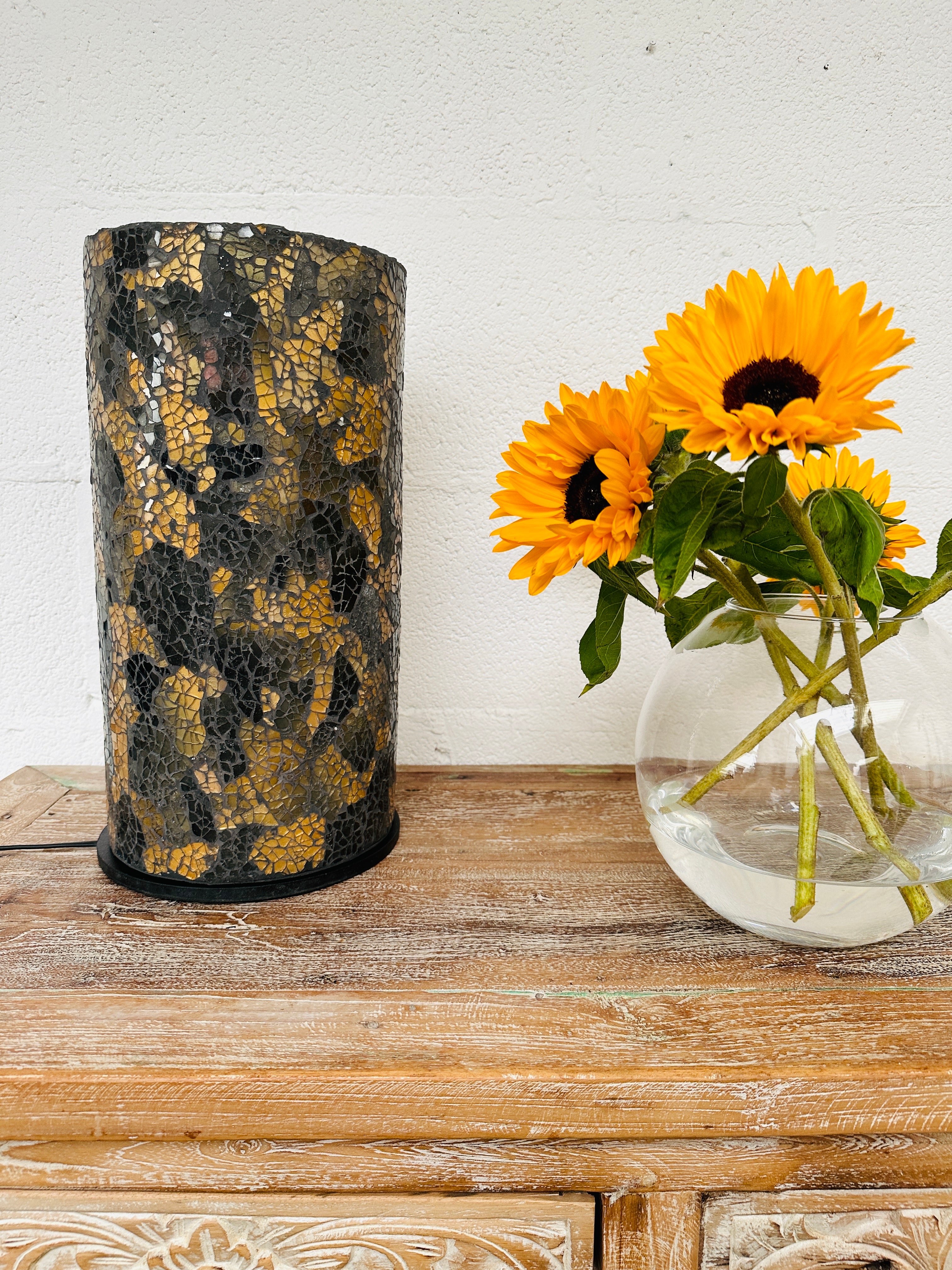 display view of mosaic cylinder lamp light off next to a vase of sunflowers
