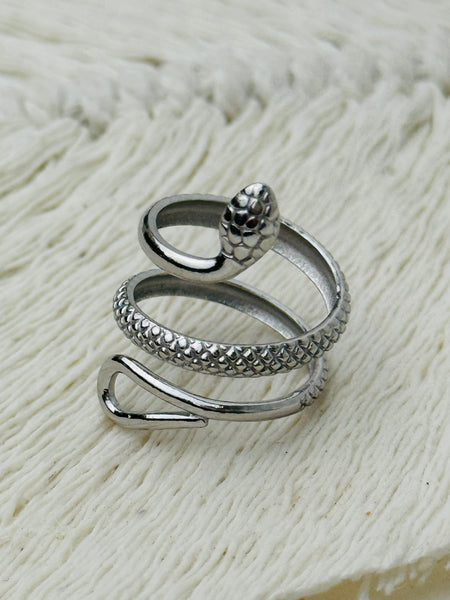 Silver serpent ring with coiled textured snake design and adjustable open band, displayed on a white fabric background.
