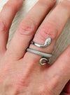 Silver serpent ring with coiled textured snake design and adjustable open band, displayed on a model.
