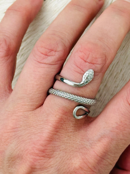 Silver serpent ring with coiled textured snake design and adjustable open band, displayed on a model.
