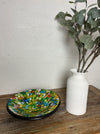 display view of mosaic glass bowl next to a vase of leaves