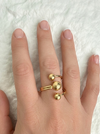 Gold ring with spherical designs on a hand against a textured white background