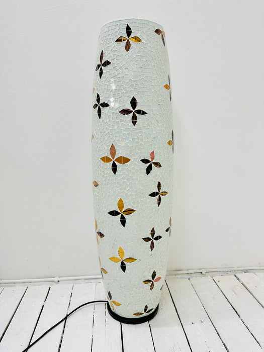 A handmade floor lamp with a fiberglass-reinforced epoxy resin base and glass mosaic in soft white tones featuring a delicate flower pattern. The lamp is switched off and photographed against a white background.