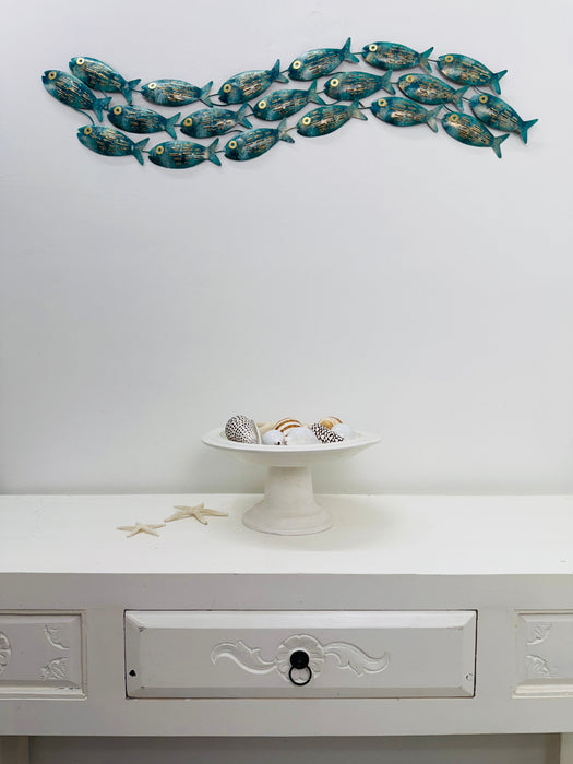 Mottled aqua metal fish shoal wall art displayed above a white side table with shells