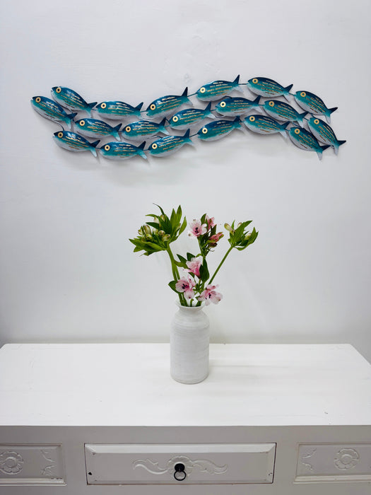 Aqua striped metal fish shoal wall sculpture displayed above a white cabinet with a vase of flowers