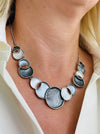 Model wearing the Aurea statement necklace with white and grey circular design.