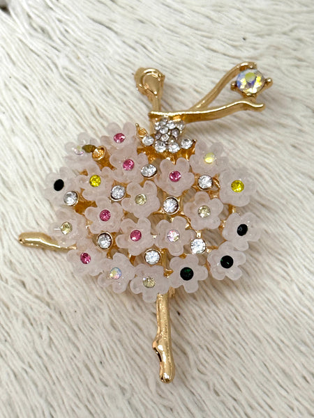 A brooch depicting a gold-coloured ballerina with a floral design, adorned with multicoloured stones