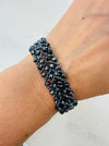 A person wearing a gunmetal-coloured beaded bracelet with a button fastening.