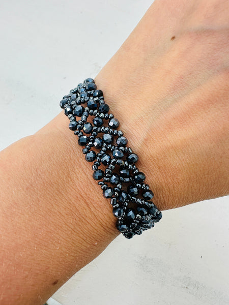 A person wearing a gunmetal-coloured beaded bracelet with a button fastening.
