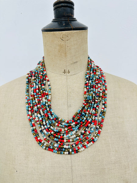 Bead statement waterfall style necklace with multicoloured seed beads and hand carved wood clasp., displayed on a mannequin.