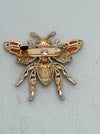 back of gold bee-shaped brooch on a light gray background
