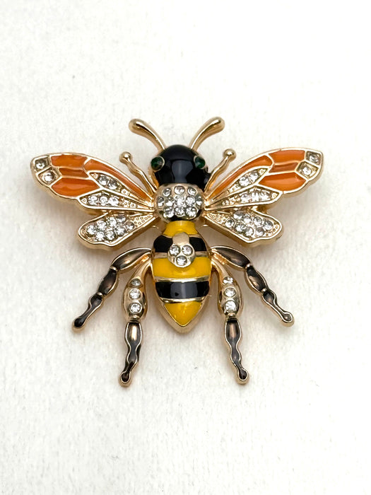 Decorative bee brooch with gold, black, and yellow colors on a white background