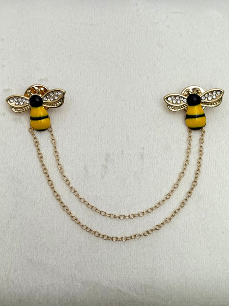 gold tone bee-shaped lapel pin with chain and crystal details on a white background
