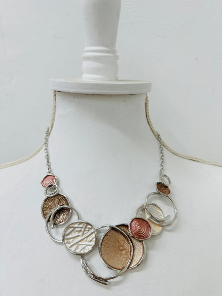 A beige enamel statement necklace with metallic accents and textured metal discs, displayed on a mannequin.