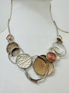 A beige enamel statement necklace with metallic accents and textured metal discs, displayed on a mannequin.