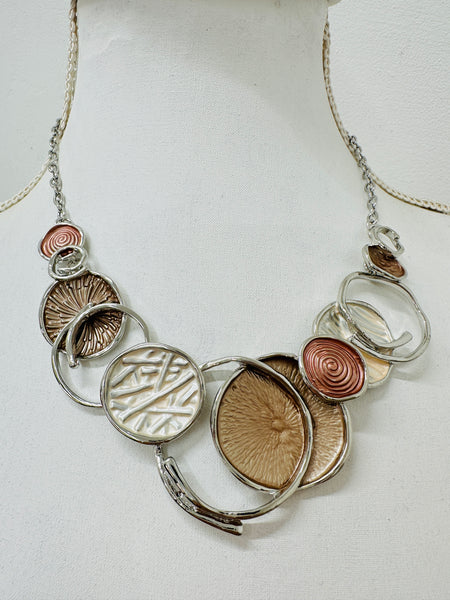 A beige enamel statement necklace with metallic accents and textured metal discs, displayed on a mannequin.