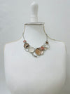 A beige enamel statement necklace with metallic accents and textured metal discs, displayed on a mannequin.