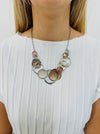 A beige enamel statement necklace with metallic accents and textured metal discs, displayed on a model.