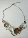 A beige enamel statement necklace with metallic accents and textured metal discs, displayed on a white background.