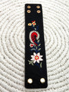 Black faux leather strap with floral embroidery on a white textured background