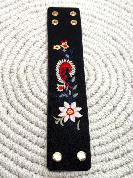 Black faux leather strap with floral embroidery on a white textured background