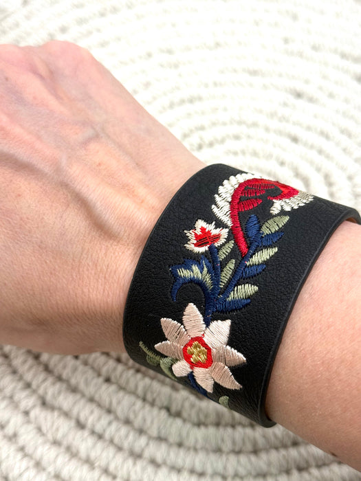Black bracelet with floral embroidery on a wrist against a textured white background