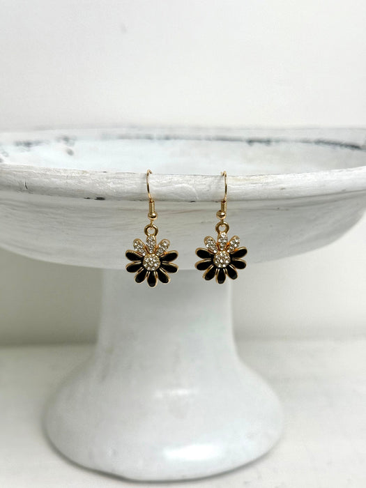 Pair of black and gold flower-shaped earrings on a white cake stand.